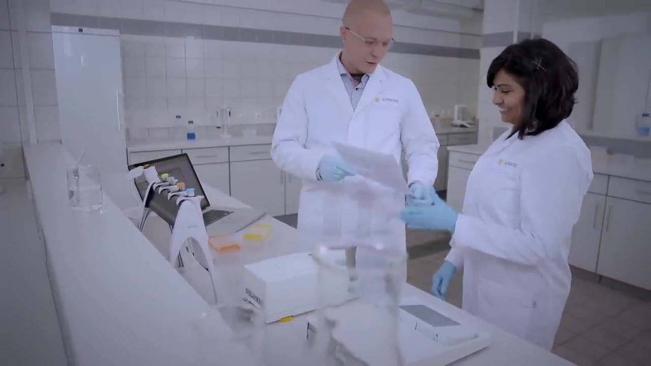 A gloved hand holding a single-channel pipette, removing it from a pipette stand in a clean laboratory environment. Other pipettes are visible in the background.