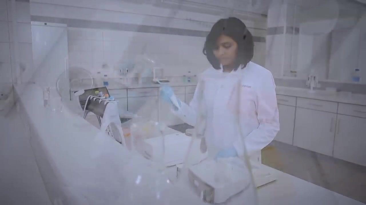 A laboratory technician in a white lab coat and blue gloves pipetting at a calibration station, maintaining a steady rhythm. The workspace is organized and clean.