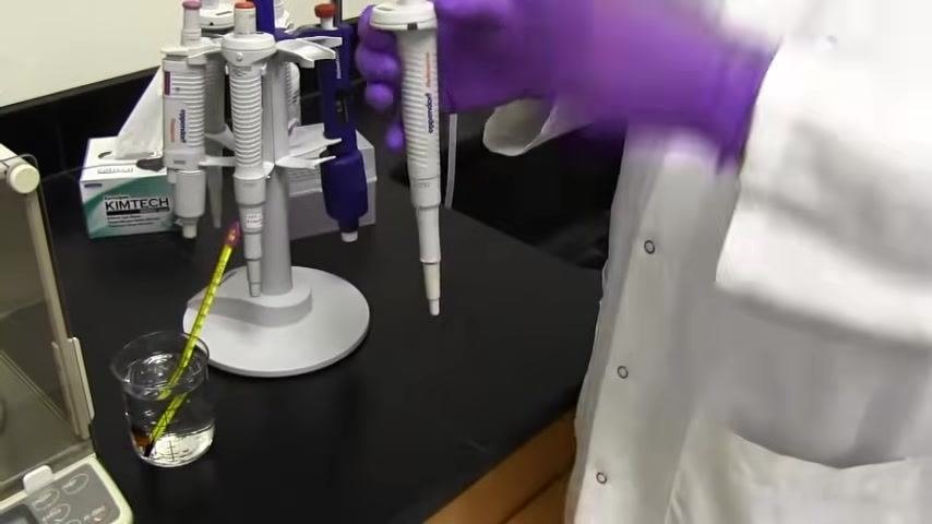 A person in a lab coat and purple gloves holds a pipette, preparing for calibration, with calibration equipment and pipette stand visible.
