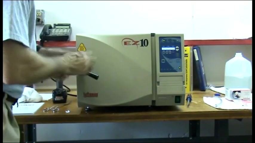 A person turning the handle to lock the autoclave door, with the control panel illuminated.