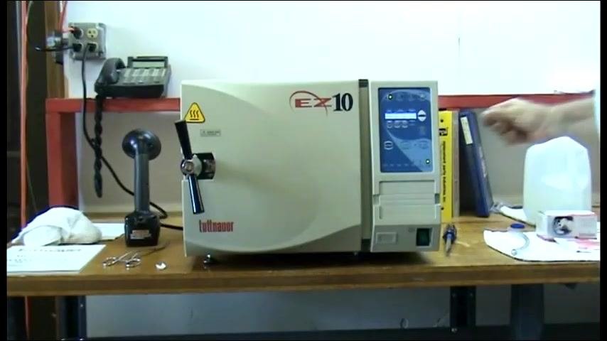 The autoclave door locked, control panel active, and a hand positioned near the panel.