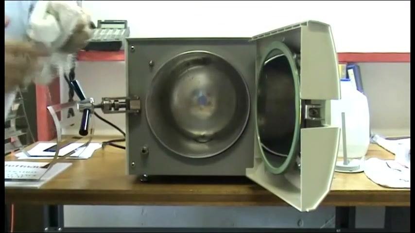 The autoclave chamber open with a person holding a cloth, ready to manage excess water.