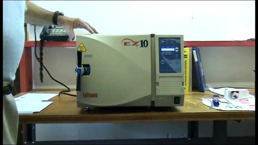 The autoclave closed and ready to be opened, with the operator's hand on the door handle and the EZ-10 unit set up on a workbench with supplies nearby.