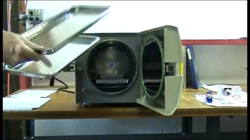 The autoclave door open with trays being removed by hand, revealing the chamber interior.