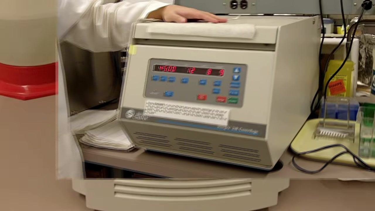 A person in a lab coat holds up a small microfuge tube, demonstrating the correct tube size for the centrifuge.