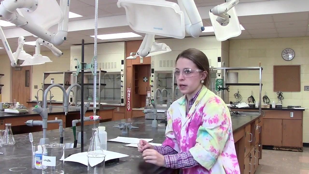 Person monitoring the titration process, with the flask on white paper and the burette dispensing solution.