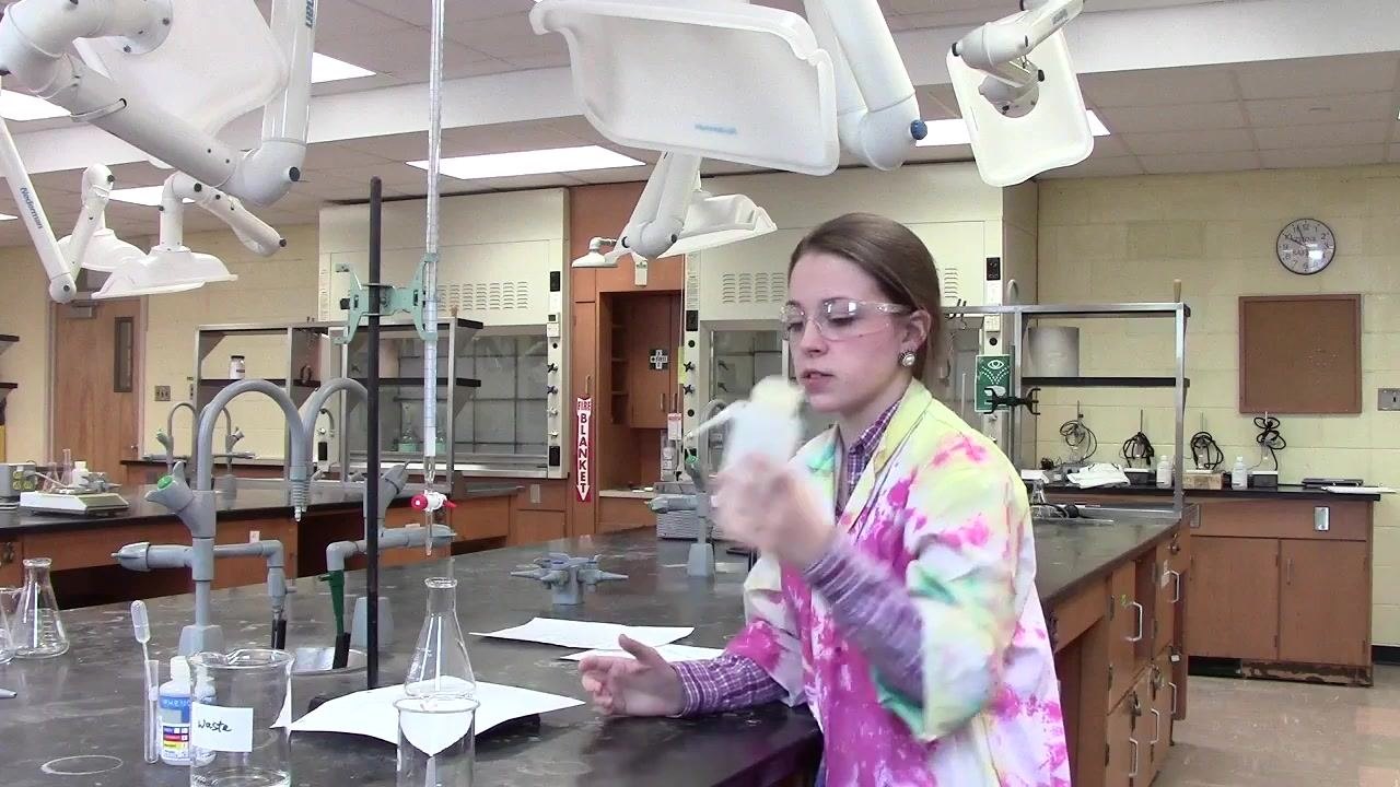 Person using a wash bottle to rinse the inside of the flask with distilled water.