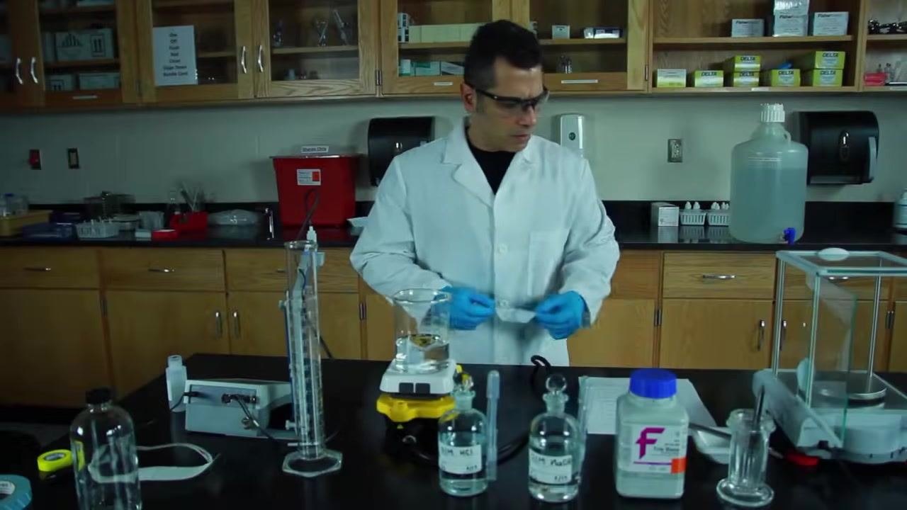 A lab-coated technician using a pH meter probe in the beaker on the stir plate, with acid and base bottles nearby