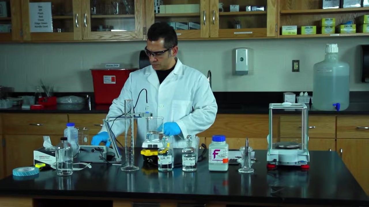 Gloved hand adding drops of 0.1 M HCl from a labeled glass bottle into the beaker, with the pH probe and other reagent bottles visible