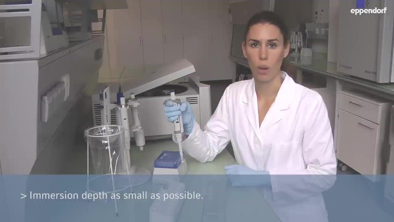 A person in a lab coat holding a pipette vertically, with a tip attached, above a tip box
