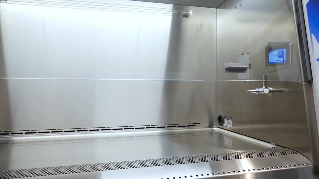 A lab worker in a white coat and gloves reviews a digital checklist on a tablet in front of the biosafety cabinet before beginning work.