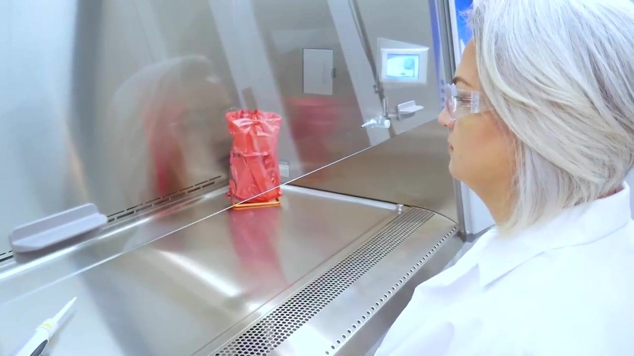 A worker uses a pipette inside the organized cabinet, with a biohazard waste container visible in the background.