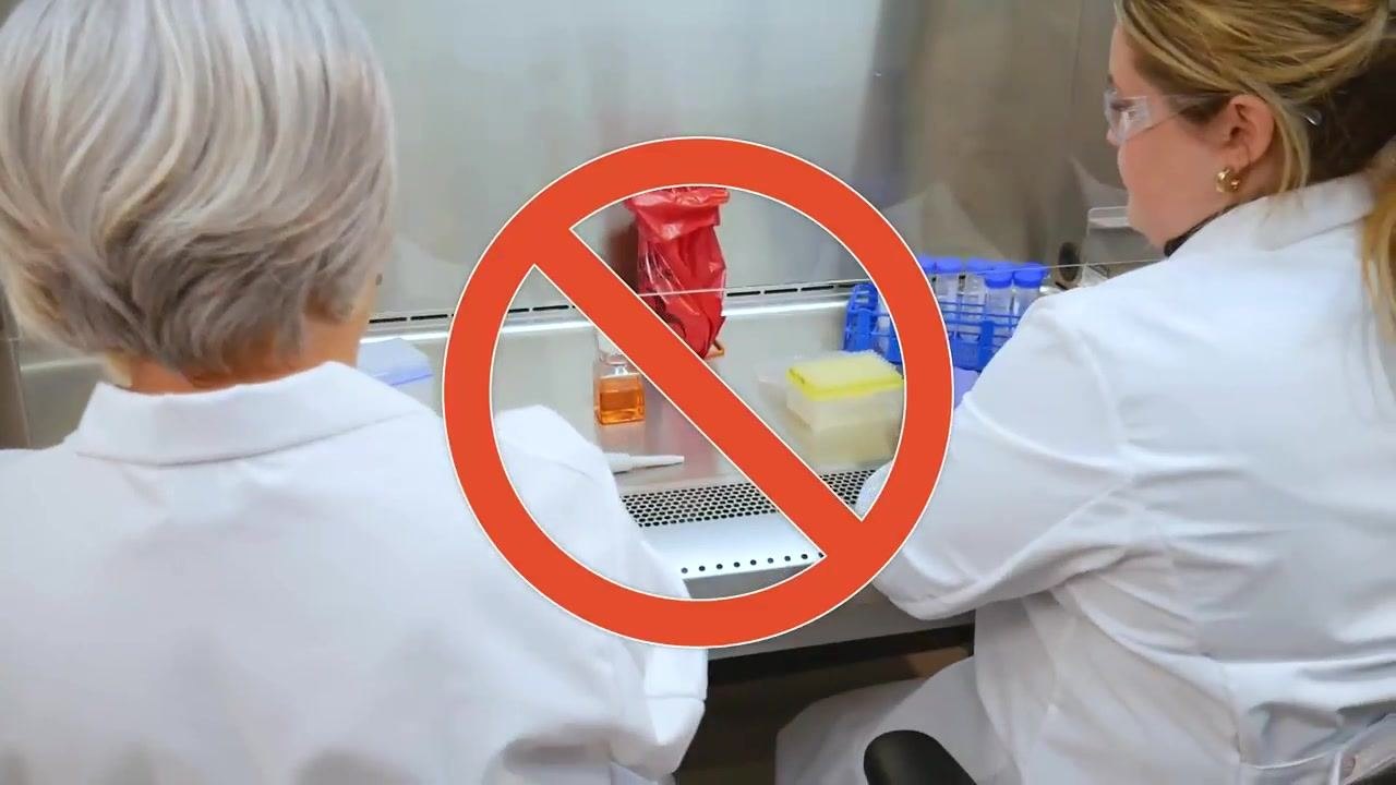 Two gloved workers handling lab equipment inside the cabinet, marked with a red "no" symbol to show an incorrect response to a spill.