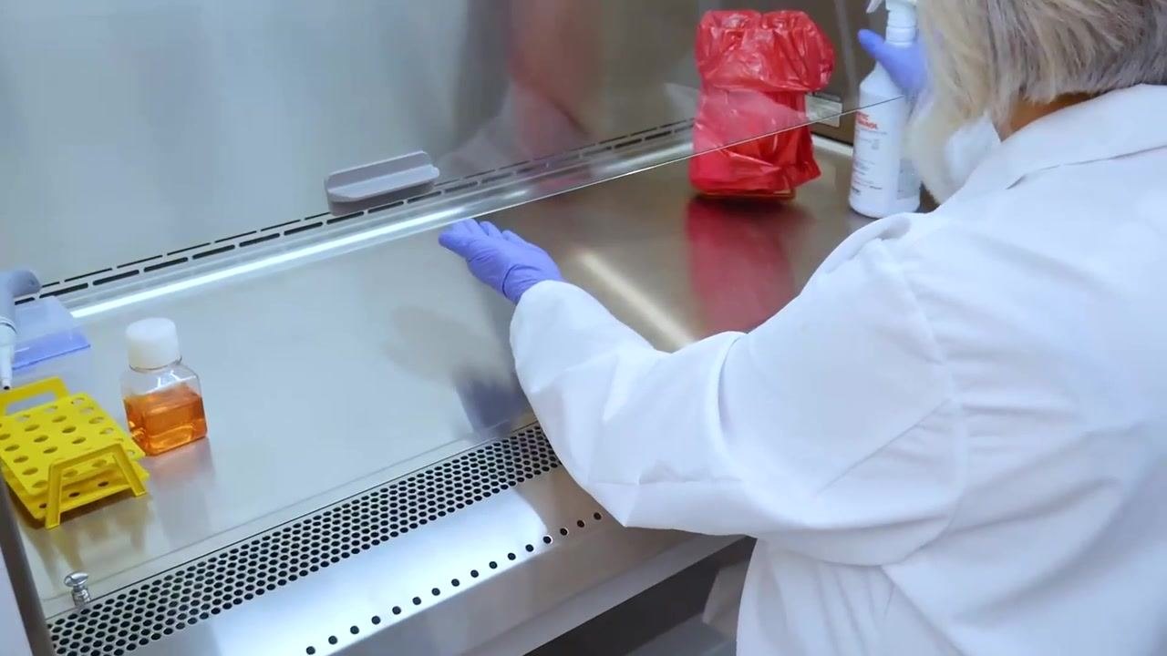 A worker wipes the entire work surface of the cabinet with disinfectant, including unaffected areas.