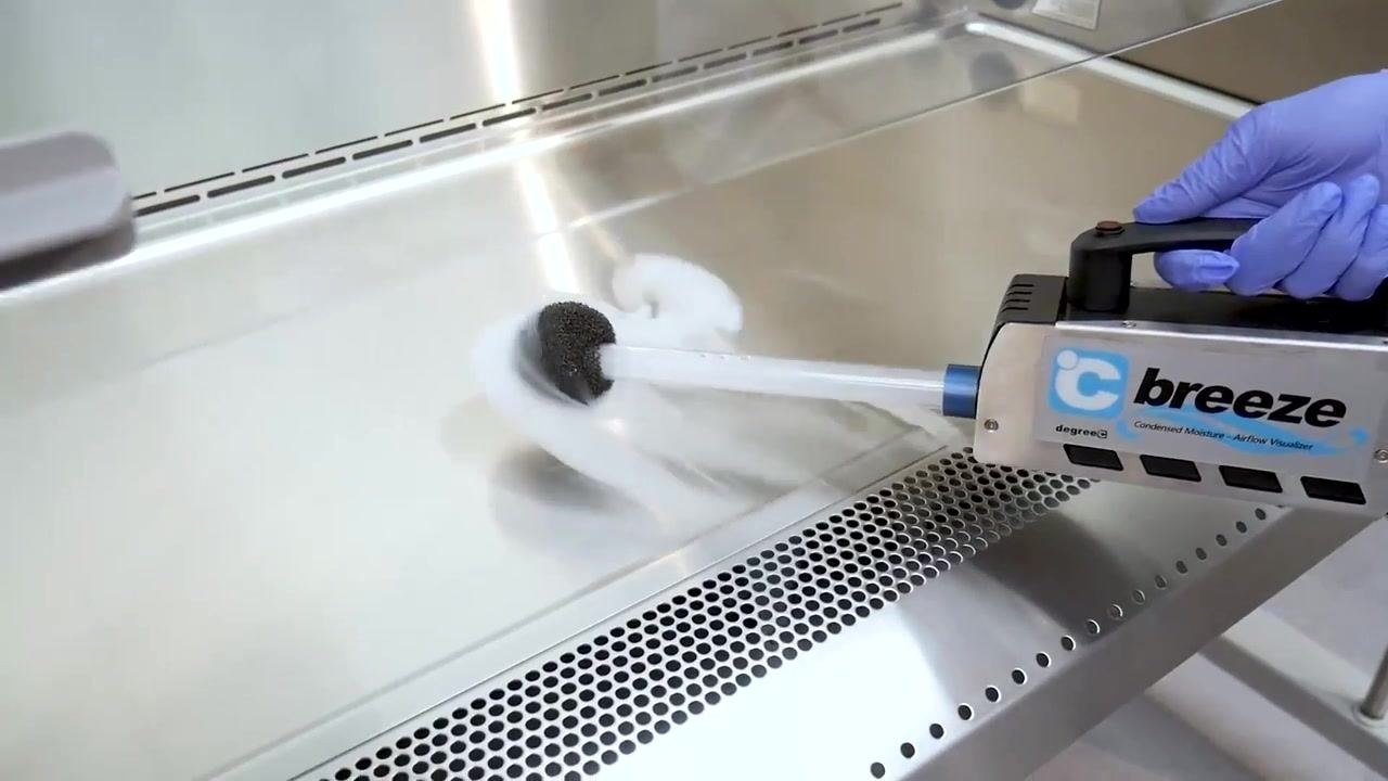 A gloved hand uses an airflow visualizer to release visible vapor, demonstrating airflow patterns above the front grille.