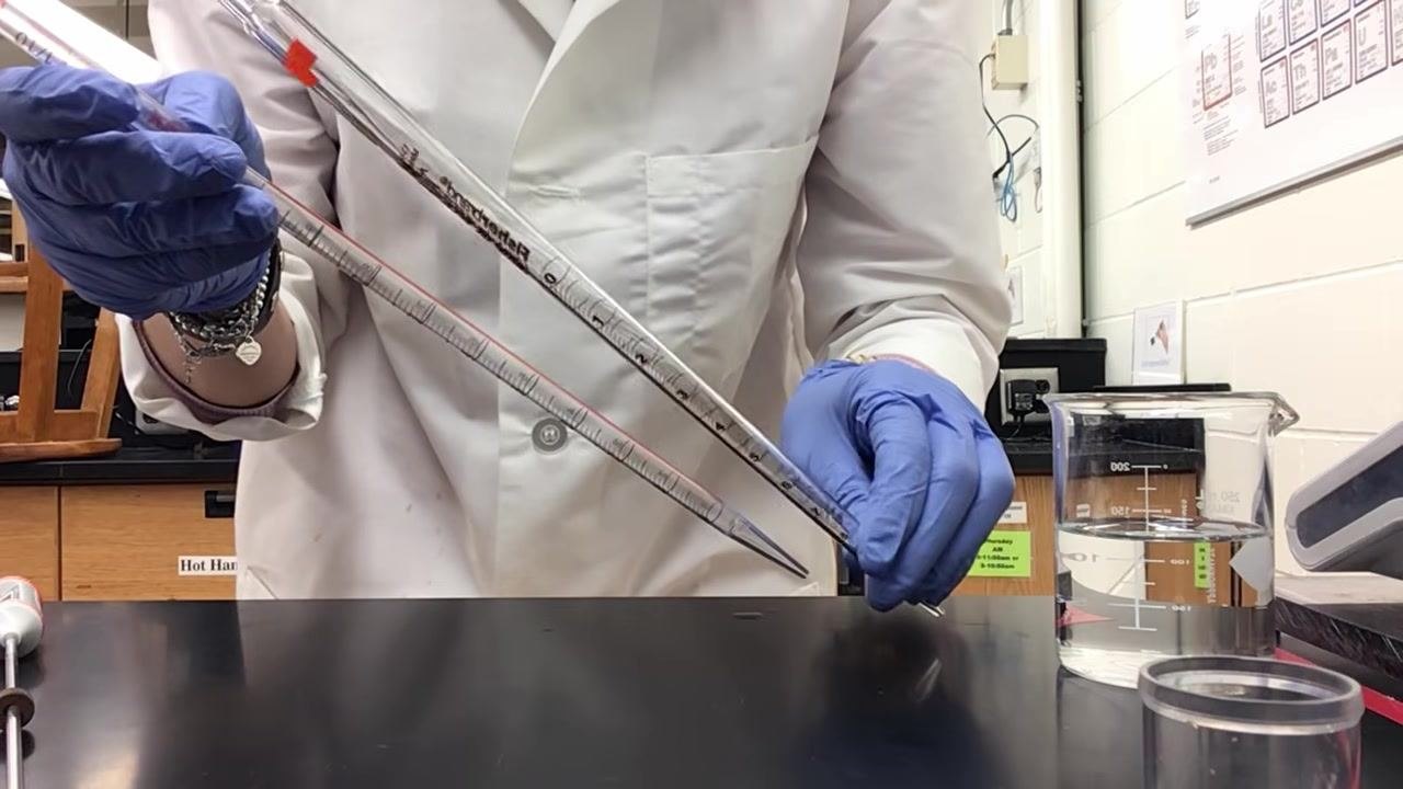 Technician holding two different pipettes side by side, highlighting differences in markings, with a laboratory background of beakers