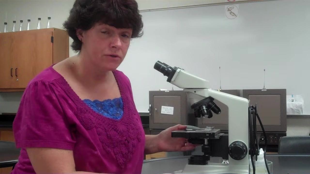 Instructor demonstrating the proper two-handed carrying technique for the microscope.
