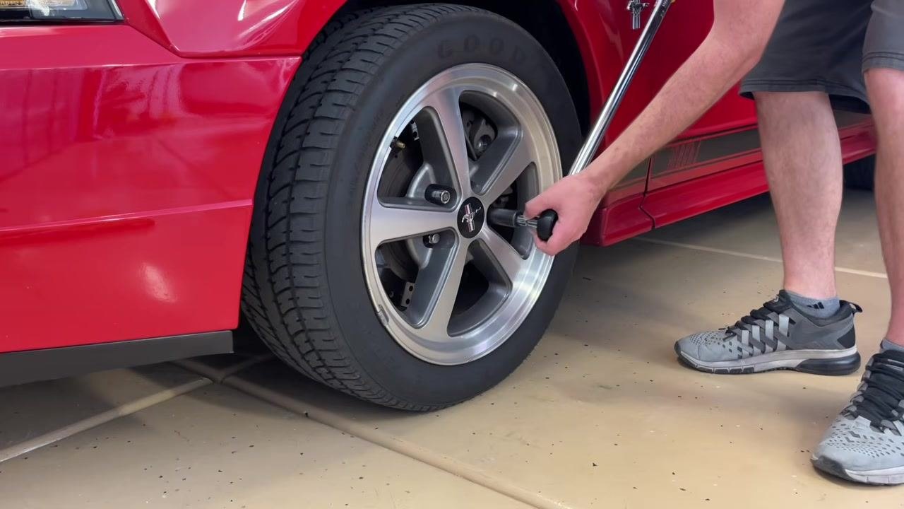 A torque wrench with a small extension and socket attached, held in front of the Mustang wheel.