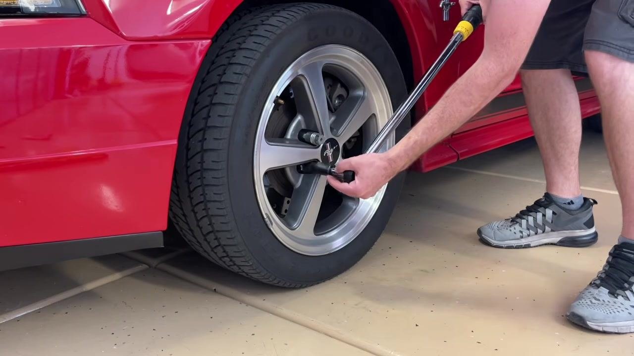 A person using a torque wrench to tighten another lug nut in a star pattern on the Mustang wheel.