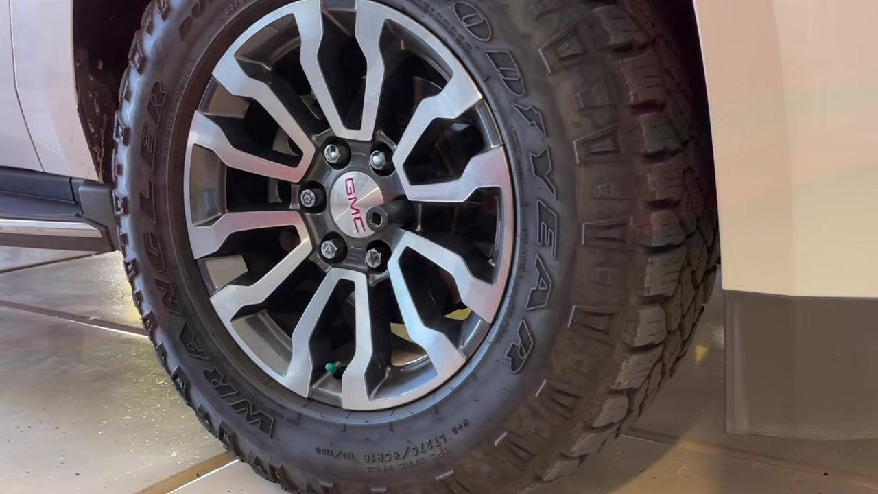 Close-up of a GMC vehicle wheel and tire, showing the lug nuts and rim before any tools are used.
