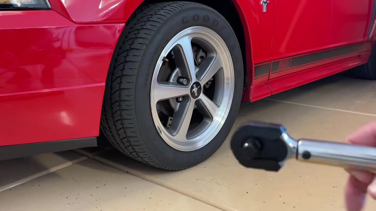 A person holding a torque wrench and a small extension bar in front of a red Mustang wheel, preparing to attach the extension.