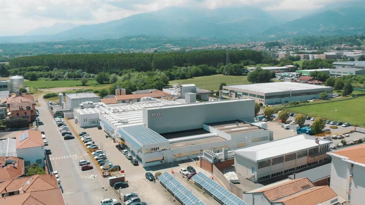 Aerial view of the Roy Electronics facility, showing the main building labeled "ROJ," parking lots, solar panels, and surrounding landscape