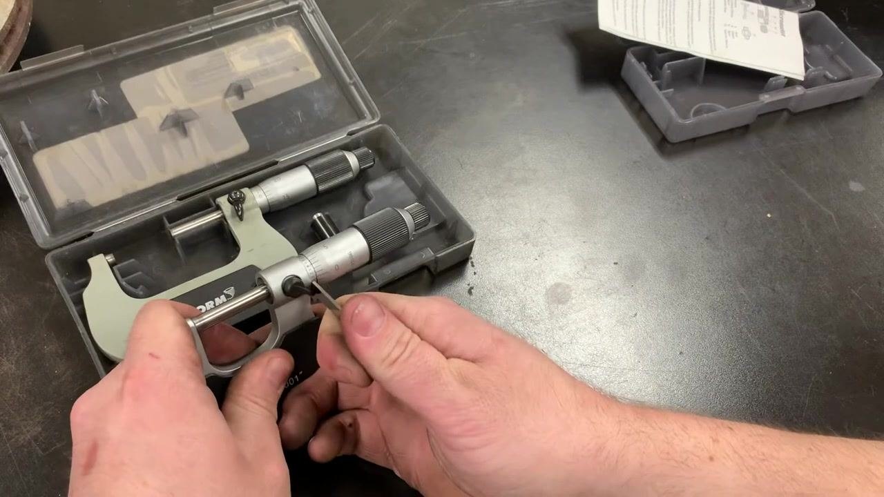 A hand inserting the spanner wrench into the adjustment hole on the micrometer sleeve