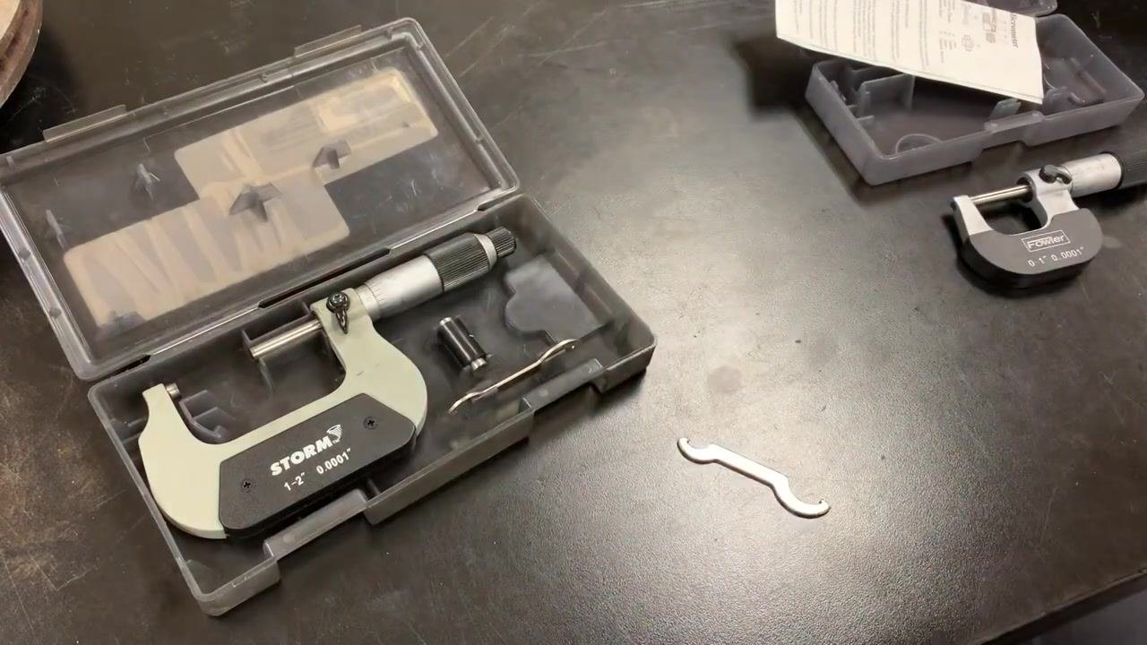 Both the STORM 1–2 inch and Fowler 0–1 inch micrometers on the workbench, with their cases open and all calibration tools and standards visible