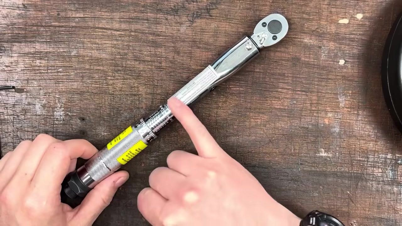 On a wooden workbench: an Allen key, a coiled rope, a torque wrench, and a 1 kg weight plate are laid out.