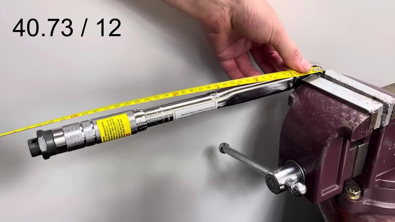A torque wrench is clamped in a bench vise, with a tape measure stretched from the center of the drive to the handle showing 11 inches. The calculation "40.73 / 12" is displayed.