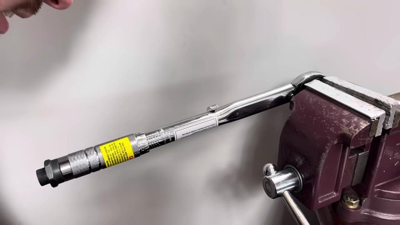 A torque wrench is clamped in a bench vise, with the handle and calibration label visible during inspection for further adjustment.