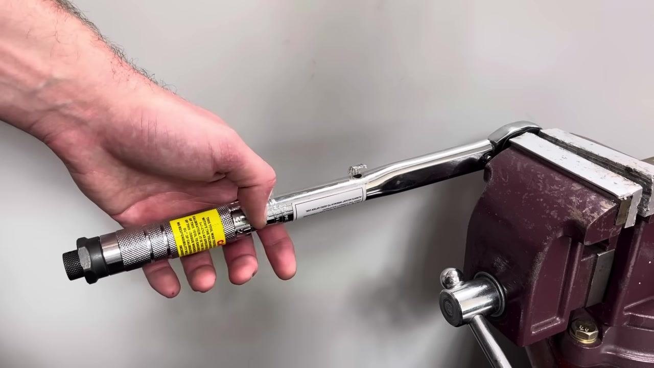 A hand holds the torque wrench handle while averaging results across multiple tests.