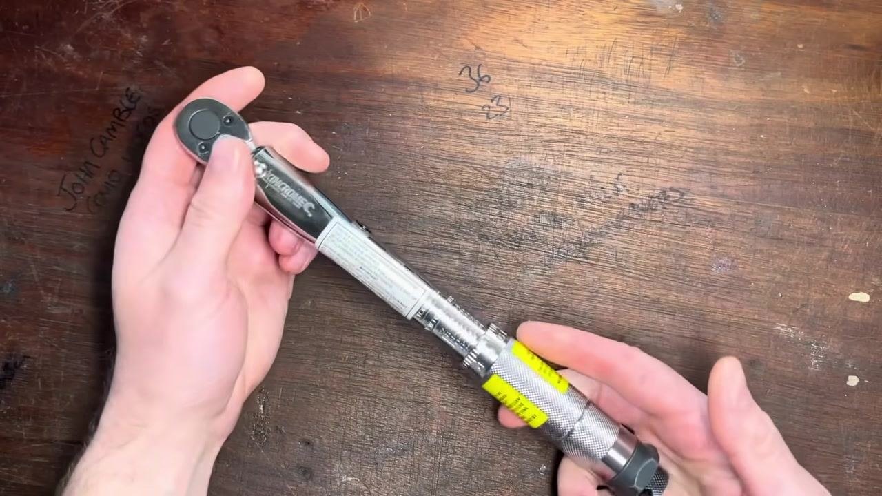 Hands hold the torque wrench on a wooden workbench, preparing to adjust the setting.