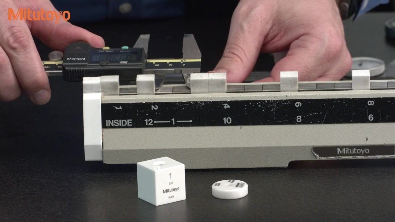 Hands using the depth bar of a digital caliper to measure on a calibration fixture, with a 1-inch Mitutoyo gauge block and calibration reference visible