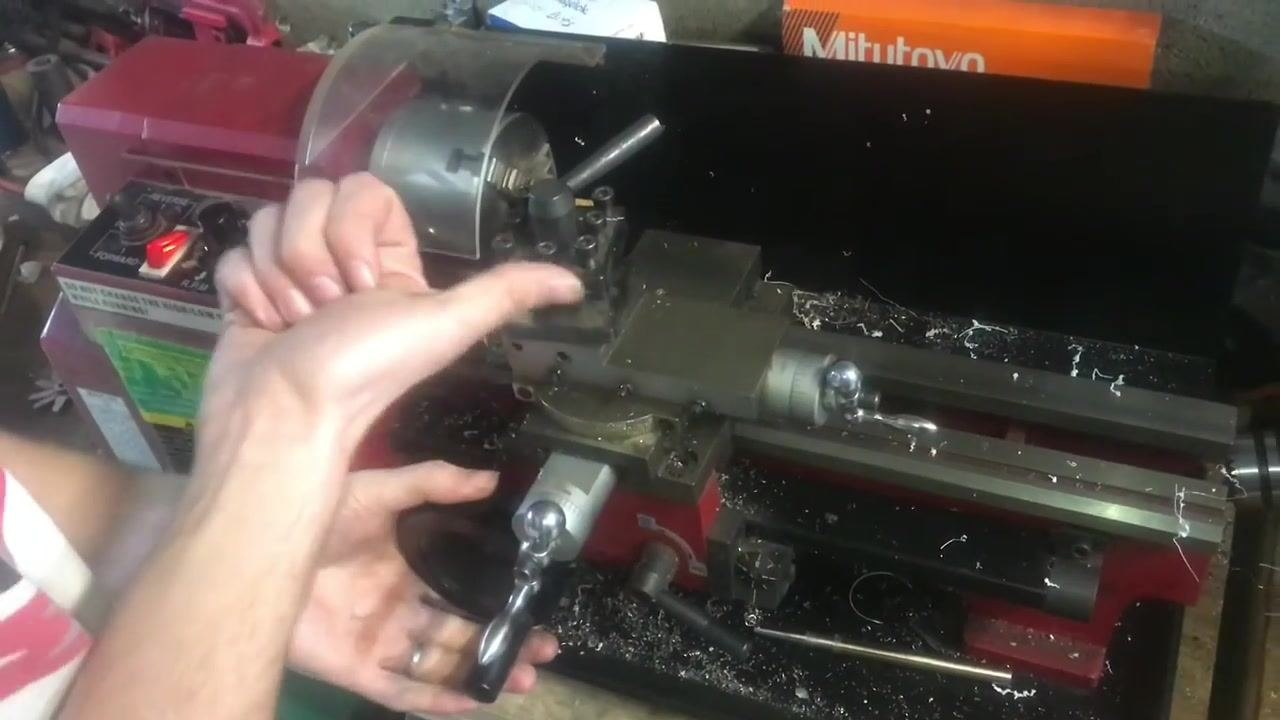 A lathe control panel with the Forward/Reverse switch illuminated, the workpiece in the chuck, the tool post in position, and metal shavings visible.