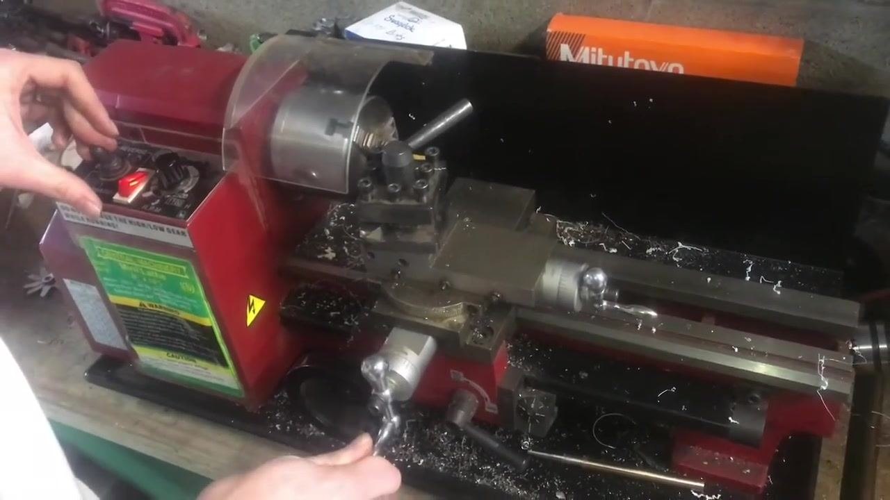 An operator's hand on the control panel and carriage handwheel, preparing to return the carriage to the starting position.