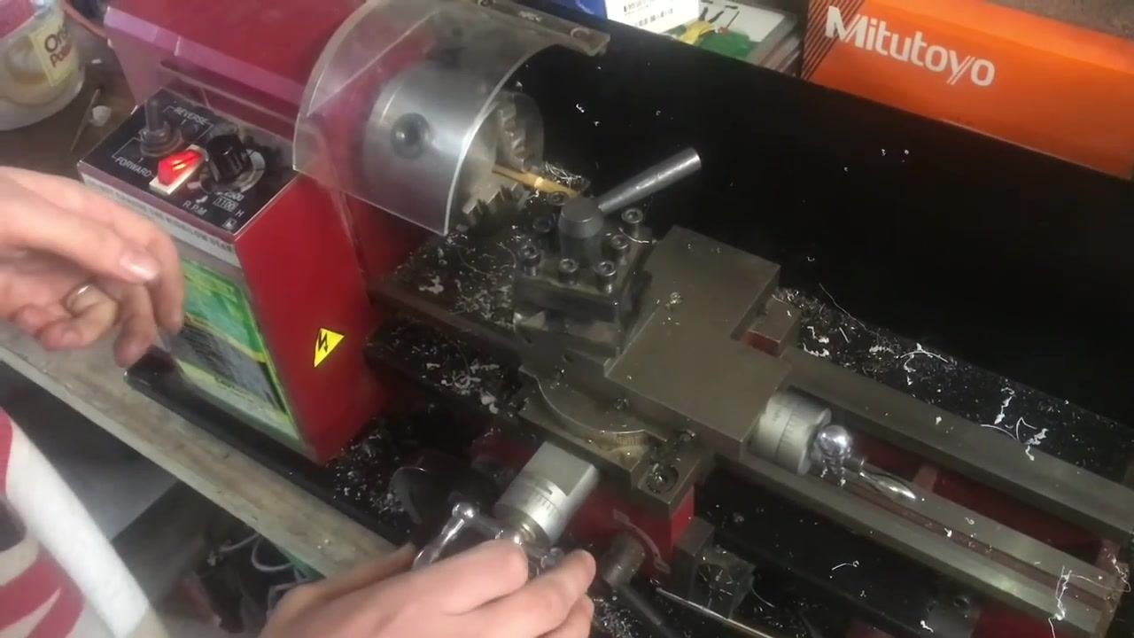 An operator's hand on the control panel, switching the lathe to Forward with the tool post and workpiece in position.