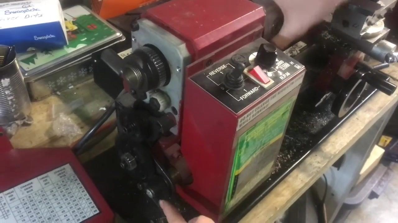 Close-up of hands holding a large bolt against the workpiece in the chuck, aligning the threading tool with the bolt's threads.