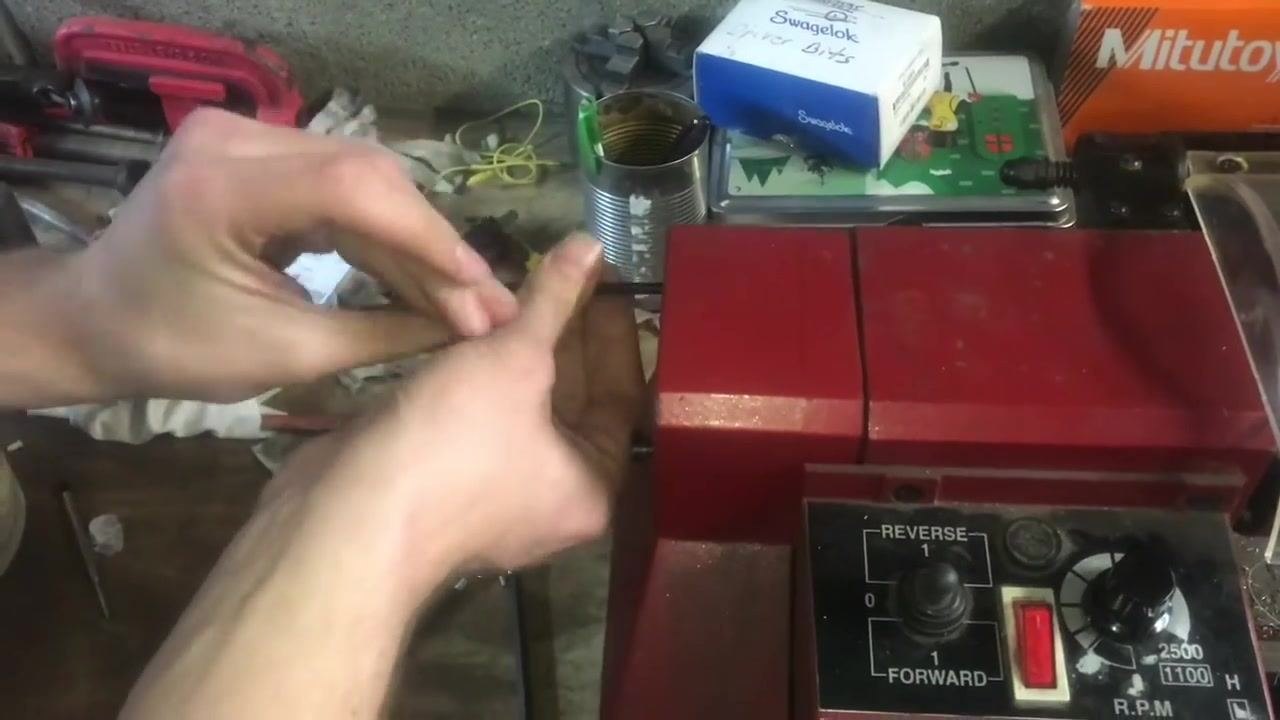 Hands holding the bolt and threading tool in position, verifying alignment with the workpiece in the chuck.