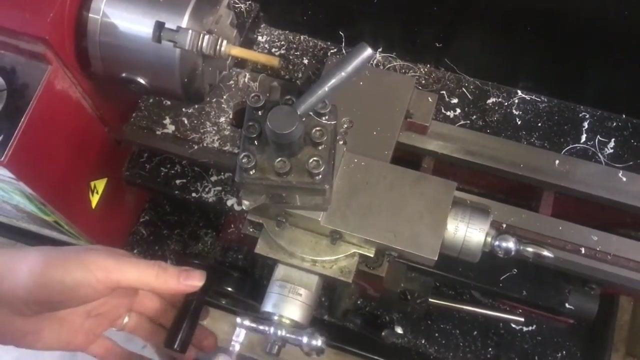 Close-up of the threading tool and bolt in the lathe chuck, with fingers pointing to the tool's position and alignment.
