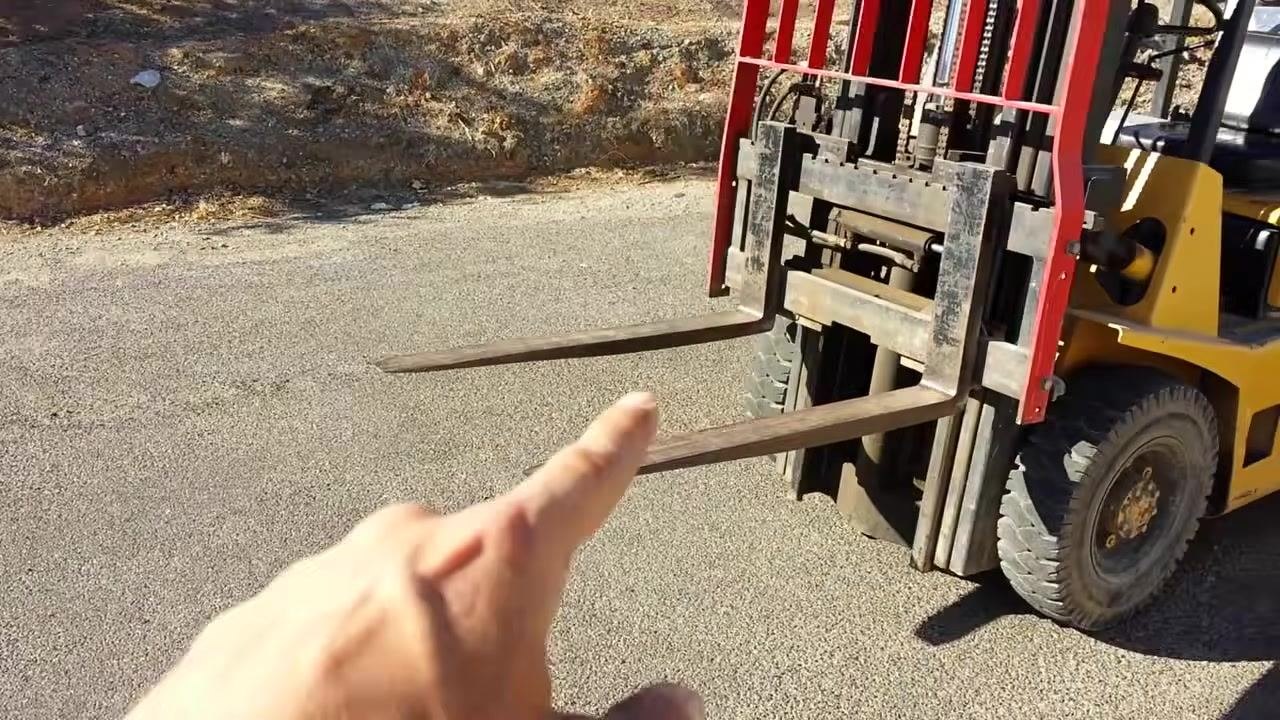 Close-up view of a forklift's forks, showing their position and structure, with a hand pointing to emphasize their function.