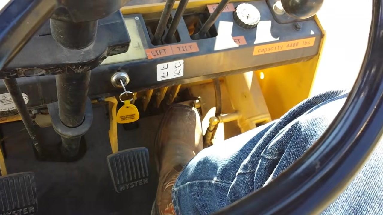 View of the operator's footwell showing two brake pedals labeled "HYSTER," the gas pedal, the ignition key, and the hydraulic control levers labeled "LIFT" and "TILT."