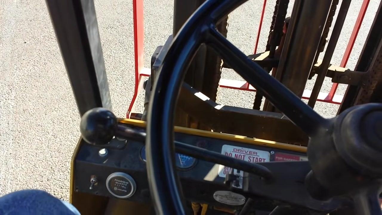 Operator's view through the steering wheel, showing the mast and dashboard as the forklift begins to move forward.