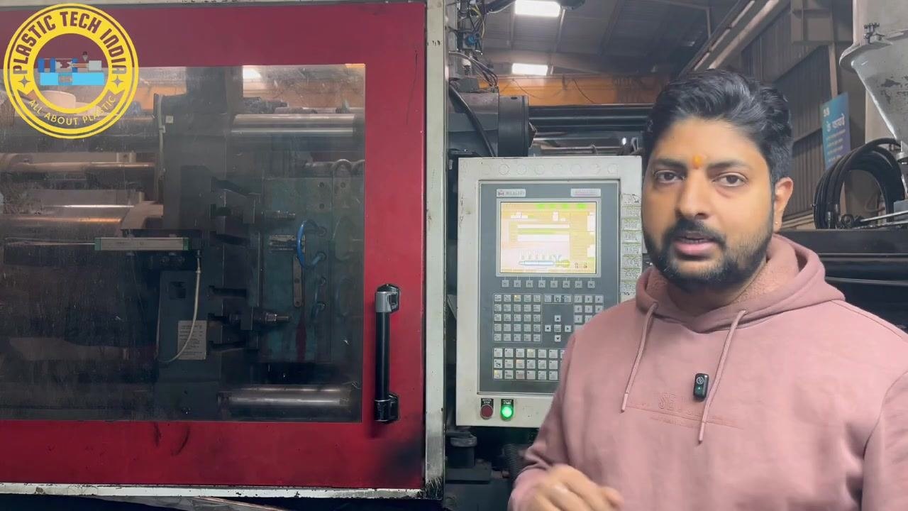 Presenter explaining the need to check the reason behind the short mold during production, standing beside the injection molding machine and control panel.