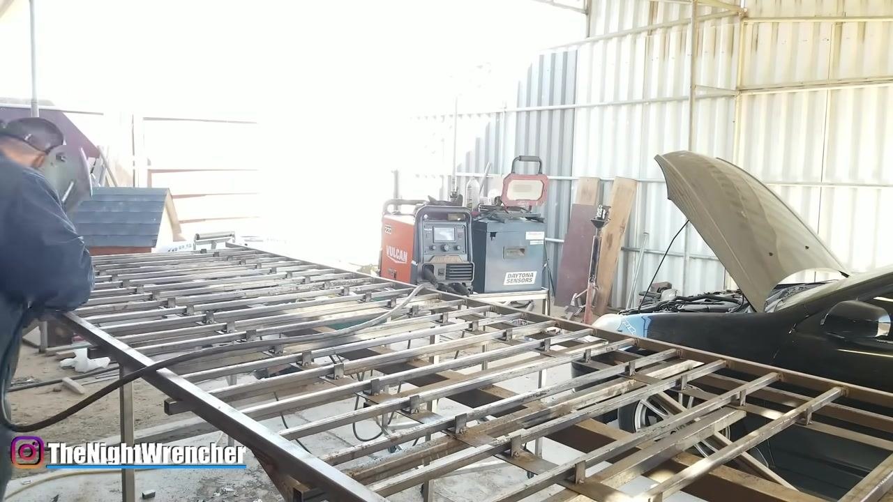 Workshop setup showing metal framework, welding machines (VULCAN ProTIG 220, Daytona Sensors), safety gear, and a car with the hood open. A large metal project is in progress.
