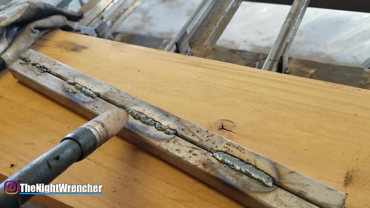 MIG gun pointing at two weld beads on metal, showing differences in bead appearance due to travel speed.