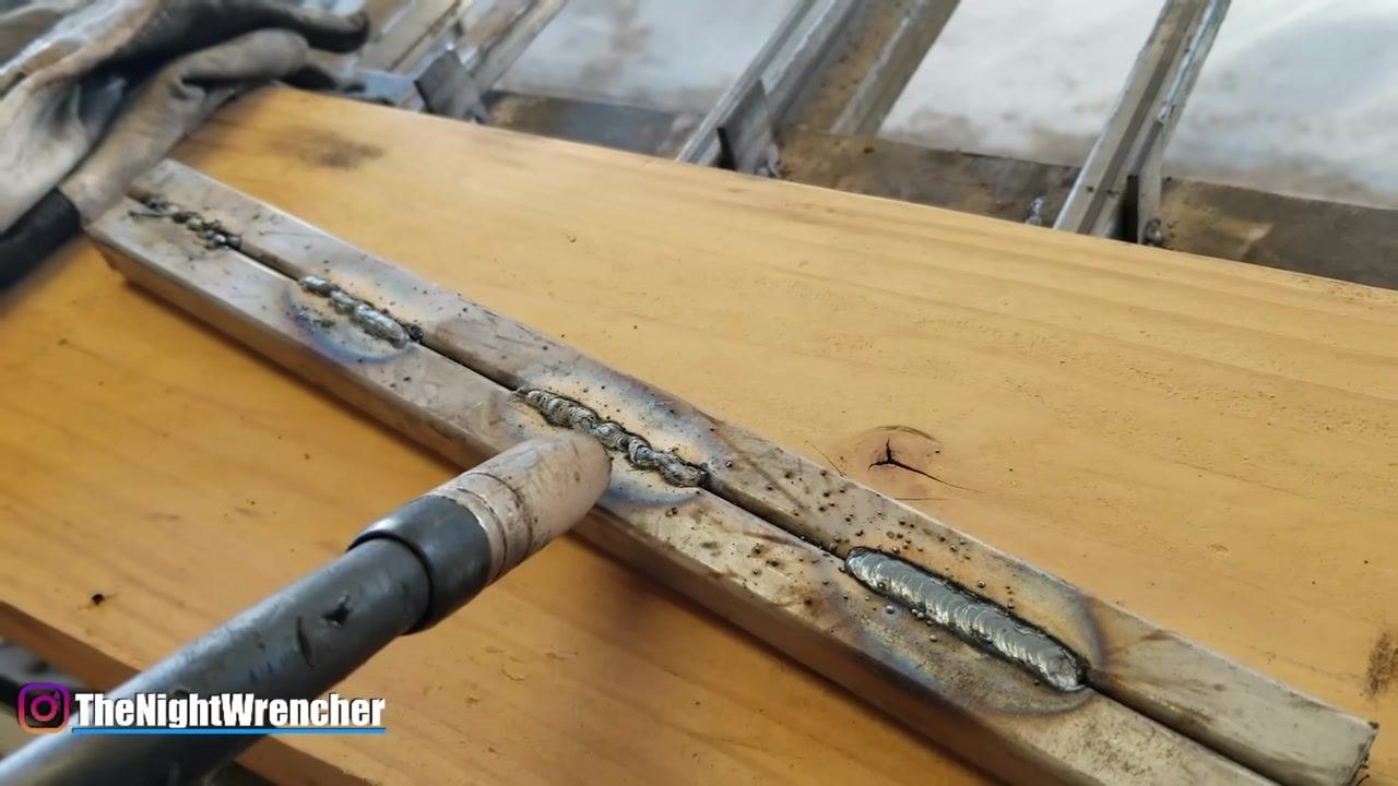 MIG gun held above two weld beads, illustrating the difference in bead quality caused by travel speed.
