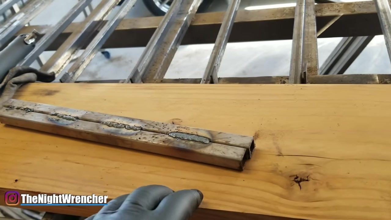 A gloved hand rests on the workbench near the welded metal bars, reinforcing the need for protective clothing during welding.