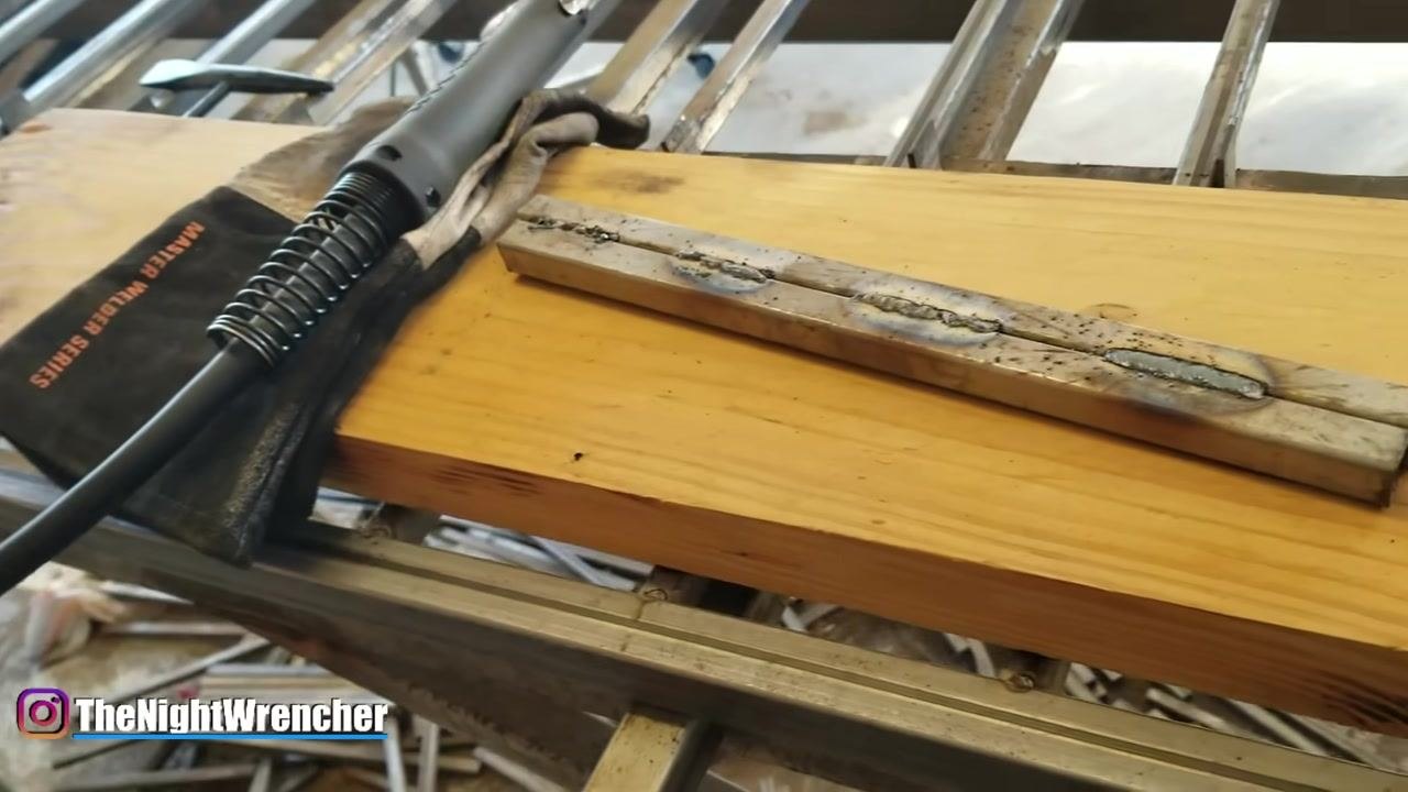 A welding torch and a pair of gloves labeled "MASTER WELDER SERIES" are placed on the wooden workbench next to the welded metal bars.
