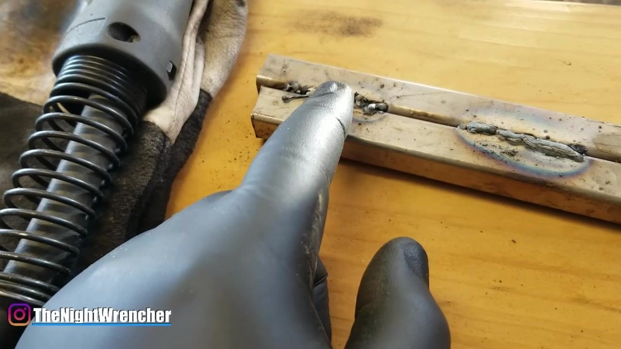 A gloved hand points at a weld bead, emphasizing the need for proper heat and material application during welding.